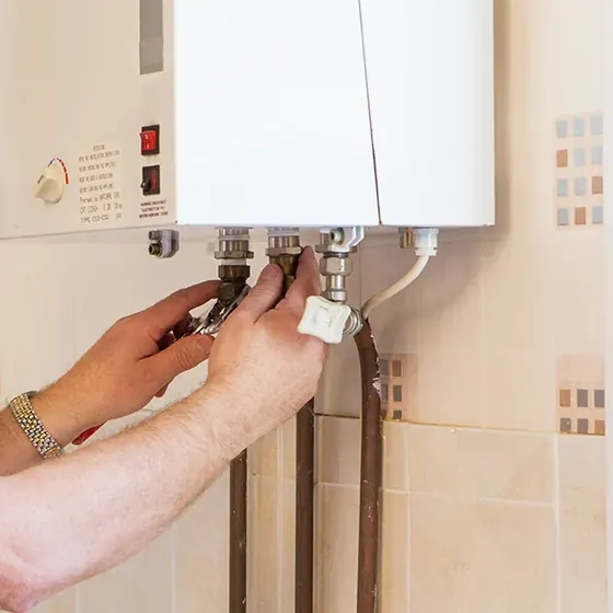 Manos de un técnico ajustando las conexiones de agua y gas bajo un calefont